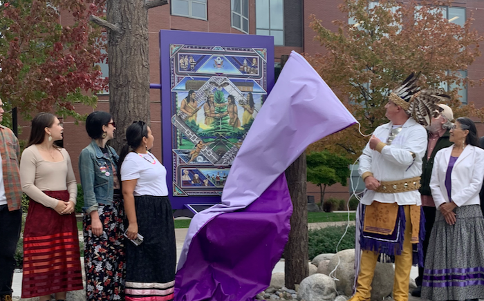 Artist Brandon Lazore pulls a purple covering off of his newly installed art work in the Shaw Quad. Bystanders are looking at the art as he reveals it.